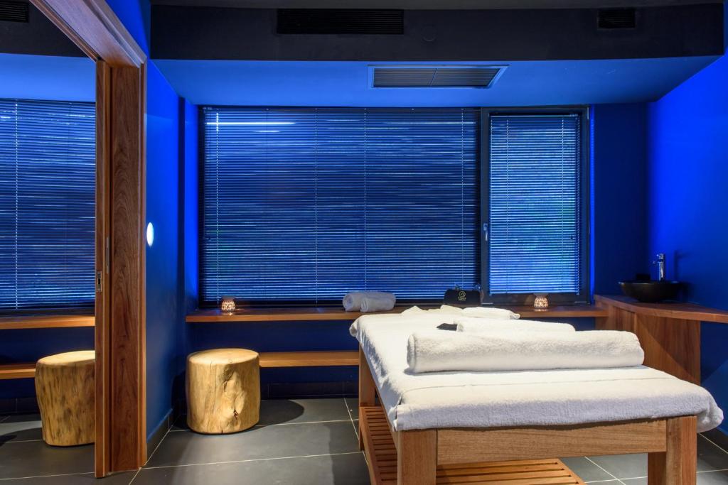 Mūsdienīgs spa telpas interjers ar zilu apgaismojumu, masāžas galdu un koka sēdekļiem, kas rada relaksējošu atmosfēru.