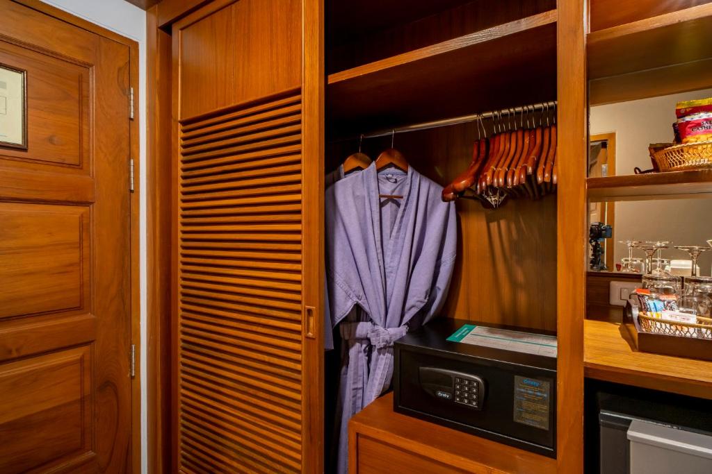 Koka skapī ir violetais halāts, apģērbu pakaramie un seifs. Blakus atrodas mini ledusskapis un glāzes uz plaukta.