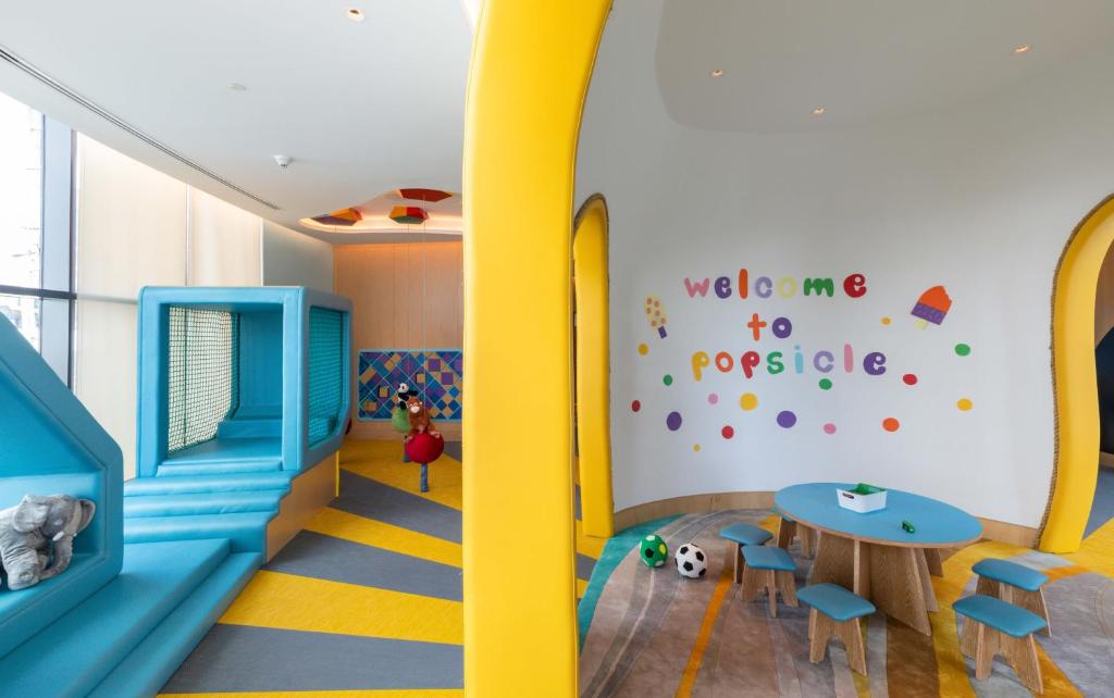 Krāsains un jautrs bērnu rotaļu stūrītis ar uzrakstu "welcome to popsicle", kur atrodas mīkstie rotaļu elementi un galdiņš ar krēsliem. Rotaļu laukums ir veidots ar spilgtām krāsām, kas aicina bērnus spēlēties un izklaidēties.