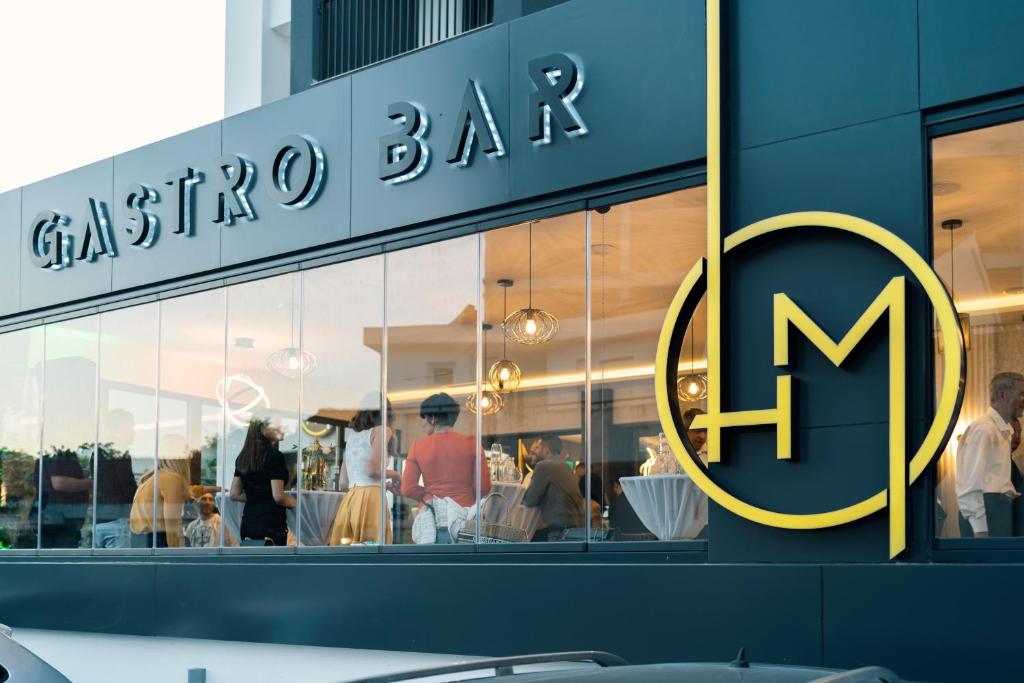 Gastro bāra modernā fasāde ar izteiksmīgu logo un redzamām apmeklētāju grupām iekšpusē.