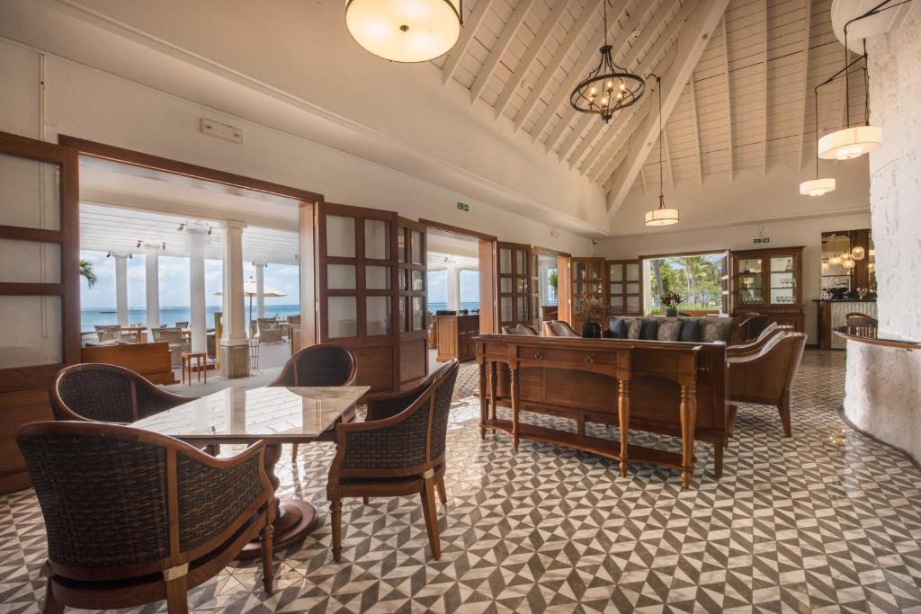 Luksusīga viesnīcas atpūtas telpa ar koka mēbelēm, plašām durvīm un skatu uz jūru. Interjers ir elegants, ar gleznainām flīzēm un gaismas ķermeņiem, radot patīkamu atmosfēru.