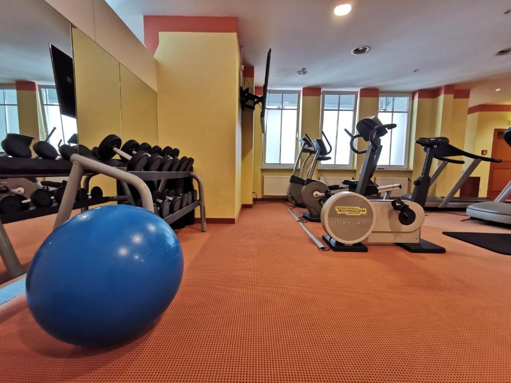 Sporta zāle ar dažādām trenažieriem, ieskaitot velosipēdu un hanteles, kā arī zilu fitnesa bumbu uz grīdas.