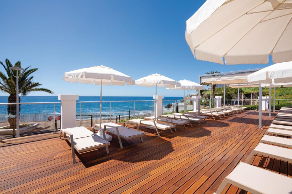 Sauļošanās zona ar guļamkrēsliem un saulessargiem pie jūras, skaidrs debesis un palmām fonā. Ideāla vieta atpūtai un relaksācijai.