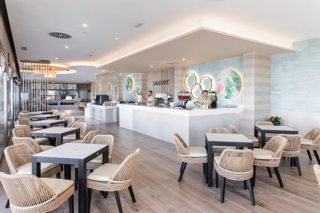 Mūsdienīgs kafejnīcas interjers ar elegantām galdām un krēsliem, gaišu apgaismojumu un dekoratīviem elementiem. Kafejnīcā redzams bārs ar dzērieniem un apkalpojošs personāls.