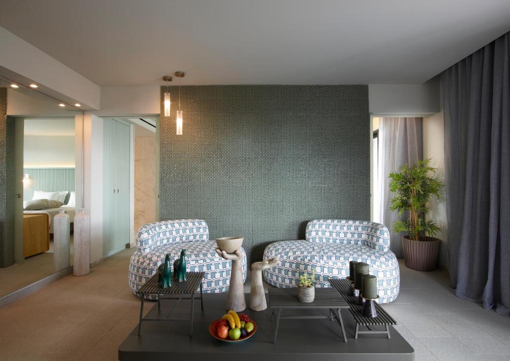 Mūsdienīgs viesistabas interjers ar stilīgām mēbelēm, zaļo sienu un izsmalcinātu apgaismojumu. Uz galda izvietotas dažādas dekorācijas un augļi, radot mājīgu atmosfēru.