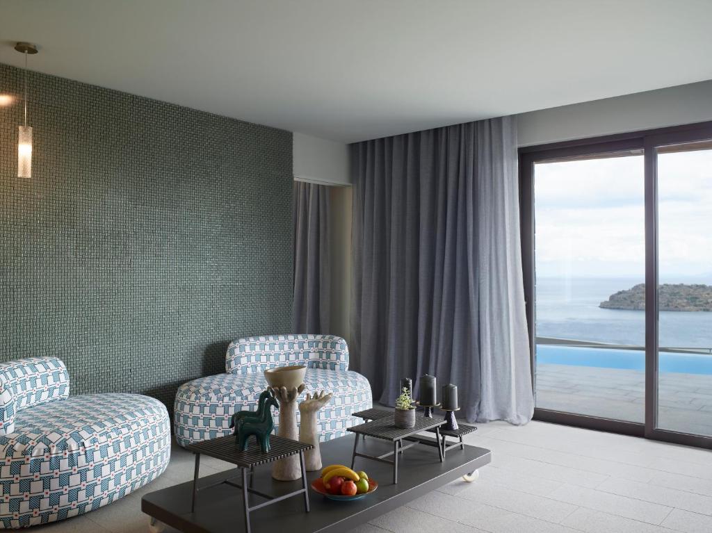 Mūsdienīgs viesistabas interjers ar krāsainiem dīvāniem, elegantām detaļām un skatu uz jūru. Gaismas un tekstūras rada relaksējošu atmosfēru.