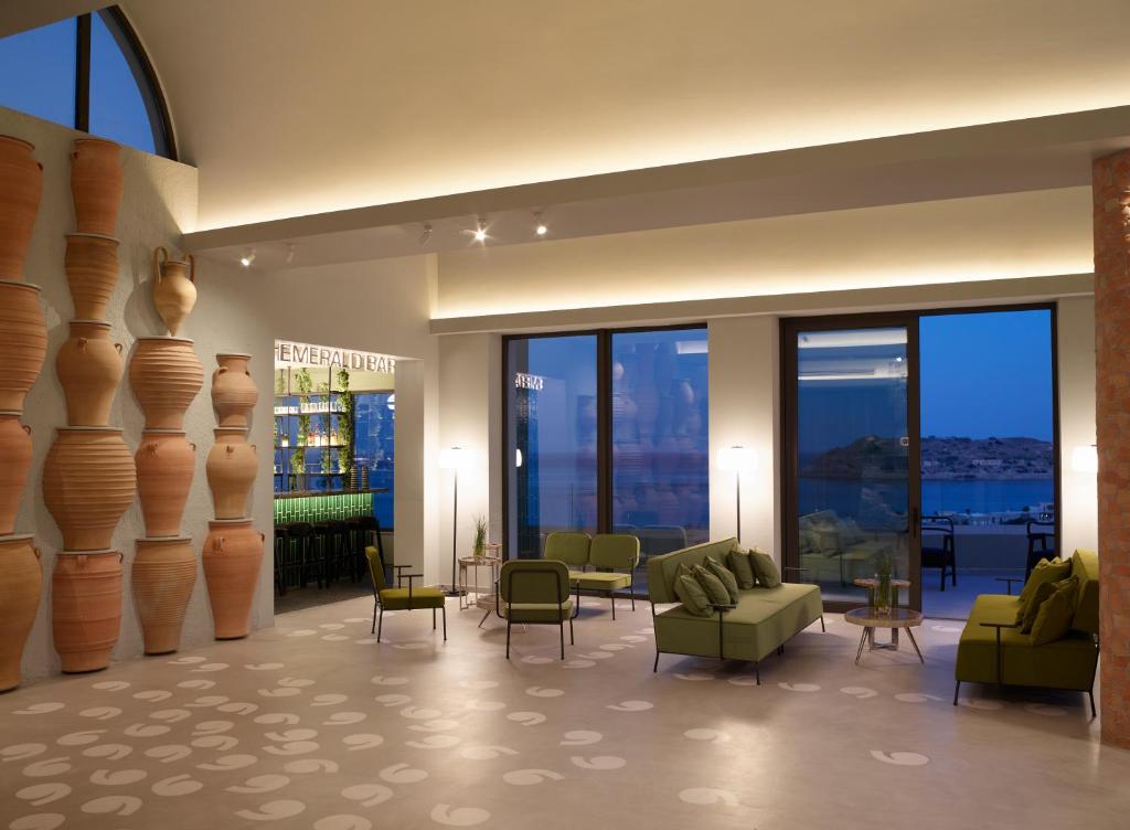 Moderns viesnīcas interjers ar zaļiem dīvāniem un keramikas traukiem uz sienas, kas rada relaksējošu atmosfēru. Skats uz jūru caur lielajiem logiem.