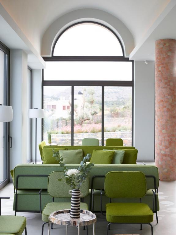 Mūsdienīgs viesistabas interjers ar zaļiem dīvāniem un krēsliem, liela loga ar skatu uz dabu. Stils apvieno komfortu un estētiku, radot patīkamu atmosfēru.