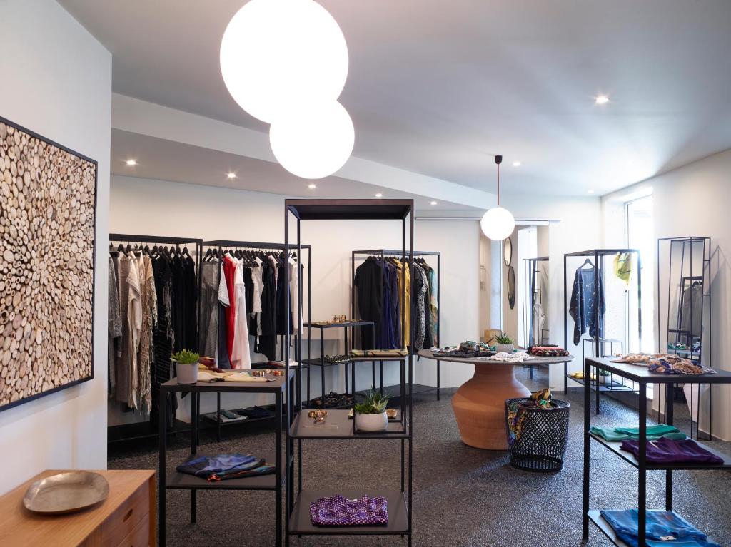 Stilīgs apģērbu veikals ar modernu interjeru, kurā redzami drēbju stendi un aksesuāri uz galdiem. Apgaismojums rada patīkamu atmosfēru.