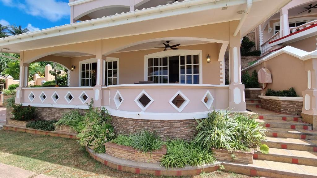 Mūsdienīga terase ar rozā krāsas fasādi, dekoratīviem elementiem un zaļiem augiem, kas rada patīkamu un viesmīlīgu atmosfēru. Skaists skats uz zilo debesu fonu.