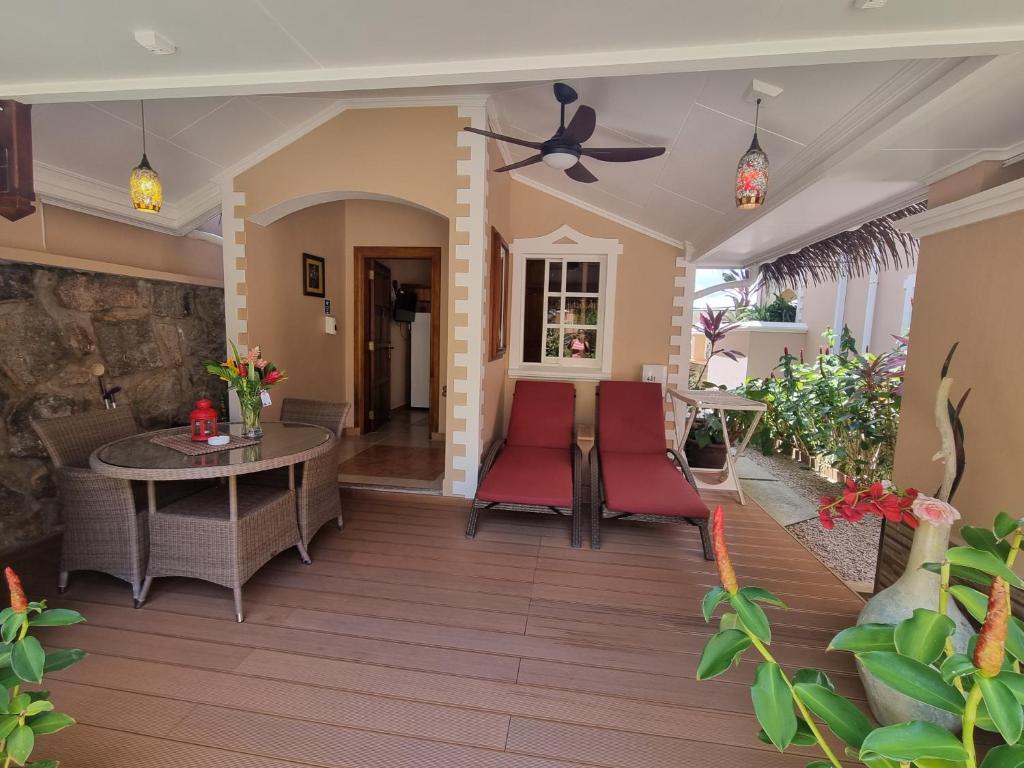 Māja ar terasi, kurā redzami divi sarkanā krāsā krēsli un apaļa galda komplekts, apjozta ar zaļiem augiem un dekoratīvām lampām. Terase ir eleganta un viesmīlīga, radot relaksējošu atmosfēru.