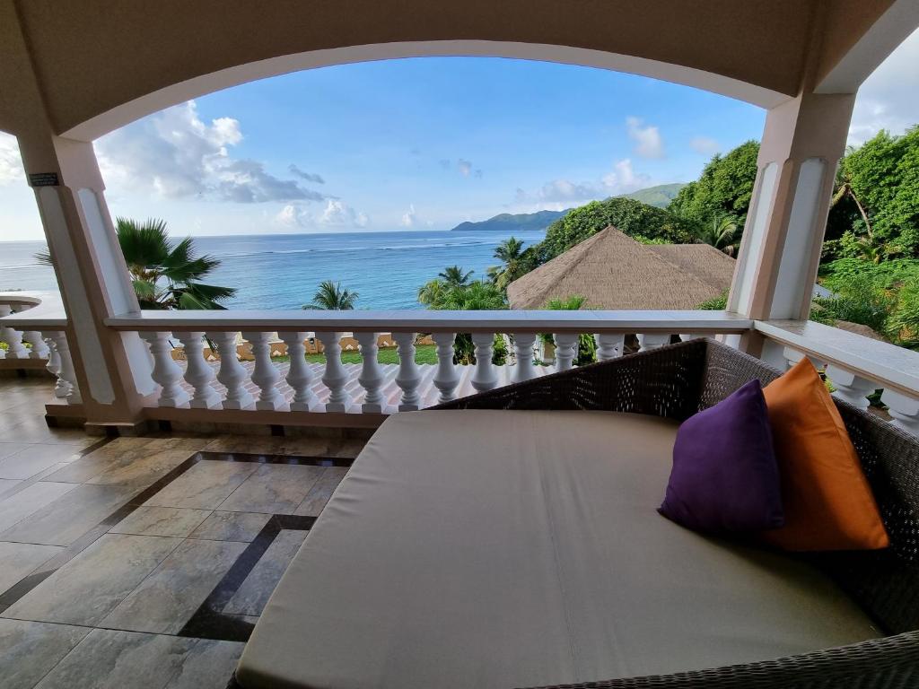 Skats no terases uz mierīgu jūru, kurā redzami palmas un kalni. Atpūtas zona ar dīvānu un spilveniem, kas rada relaksācijas atmosfēru.