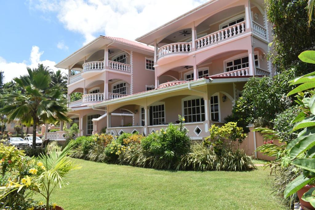 Eleganta rozā villas ar plašiem balkoniem un zaļu dārzu apkārtējo ainavu. Mājīga atmosfēra un tropu veģetācija veido relaksējošu vidi.