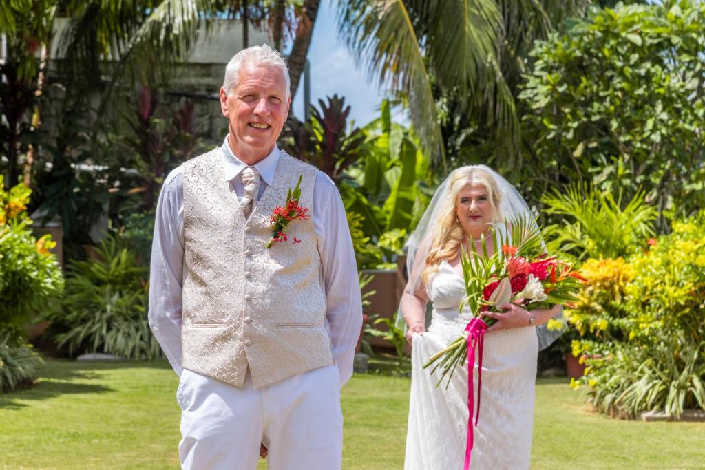 Jaunlaulātie stāv dārzā, apņemti ar sulīgu zaļumu un ziediem, svinot savu mīlestību. Vīrietis ir ģērbies eleganti, bet sieviete tērpta baltā kleitā ar pušķi rokās.