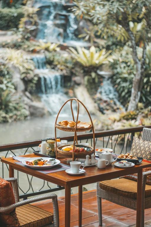 Greznas brokastis ar dažādiem ēdieniem un dzērieniem, novietotas pie galda ar skatu uz ūdens kritumu un zaļu dabu.
