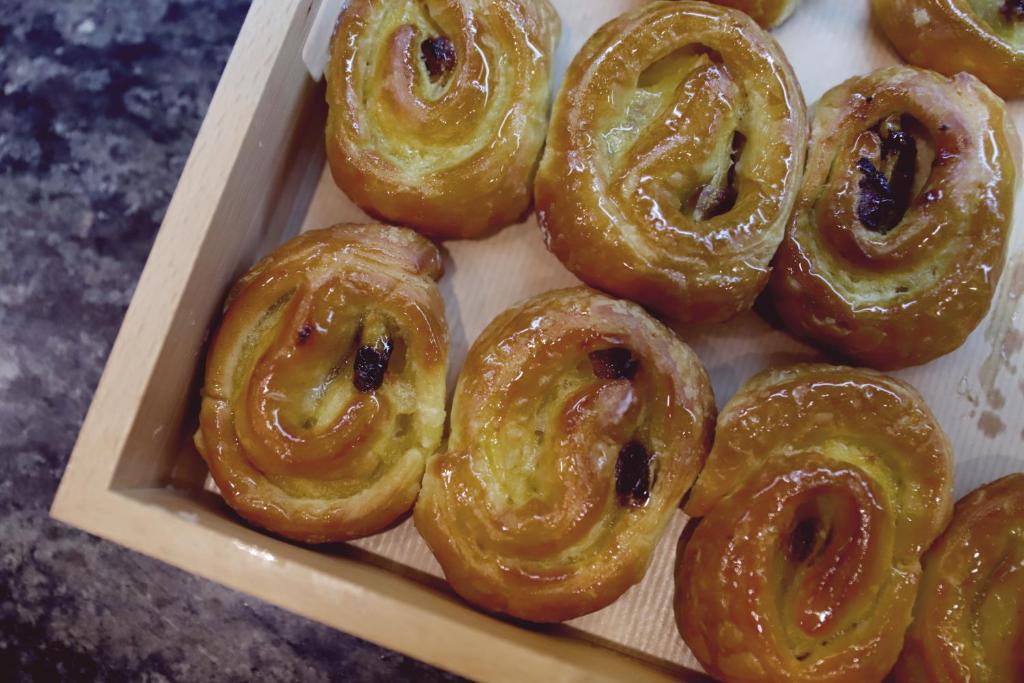 Saldie ruļļi ar glazūru un rozīnēm, pasniegti koka traukā. Ideāli piemēroti brokastīm vai uzkodām.