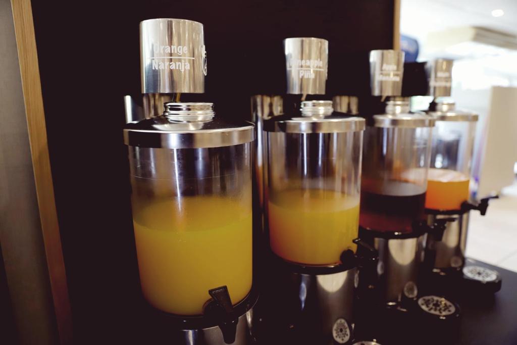 Sulu tvertne ar dažādām sulām, tostarp apelsīnu, ananāsu un ābolu. Sulas ir pasniegtas caurspīdīgās traukos ar metāla vāciņiem.