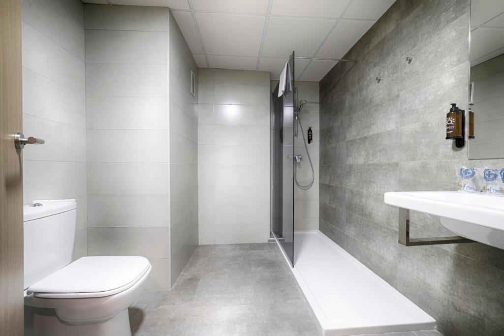 Mūsdienīgs vannas istabas interjers ar dušu, tualeti un minimālistisku dizainu. Telpa ir gaiša un eleganta, ar pelēkām flīzēm un modernām iekārtām.