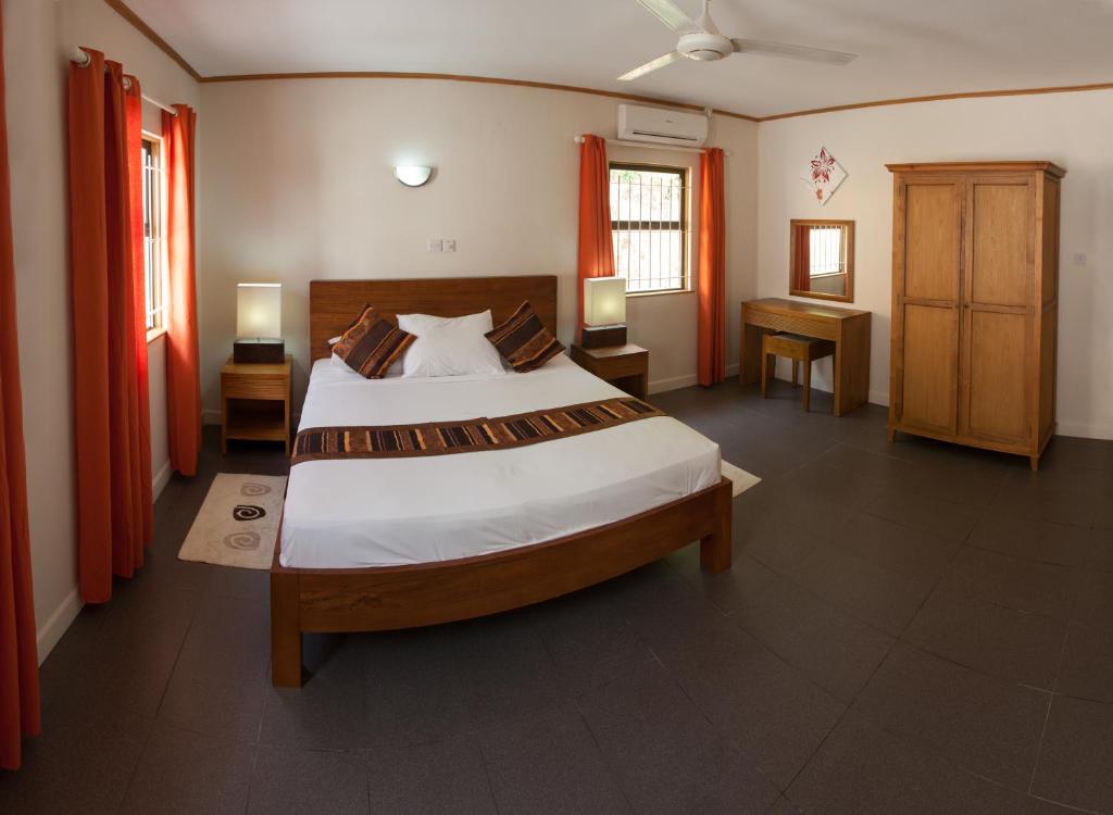 Mūsdienīgs guļamistabas interjers ar gultu, koka mēbelēm un siltām krāsām, kas rada mājīgu atmosfēru. Telpā ir arī logi ar aizkariem un gaismas avoti, kas papildina telpas apgaismojumu.