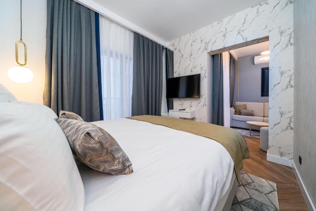 Mūsdienīga guļamistaba ar elegantu dizainu, kurā ir ērta gulta, televizors un atpūtas zona. Telpā ir gaišas krāsas, stilīgas aizkaru un apgaismojuma detaļas.