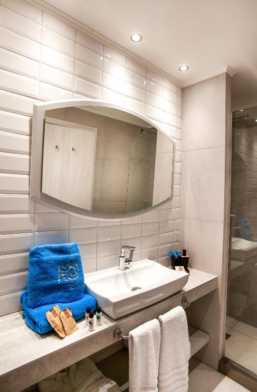 Mūsdienīgs vannas istabas interjers ar apaļu spoguli, izsmalcinātu izlietni un zilu dvieli. Uz letes ir dažādi vannas piederumi un kosmētika.