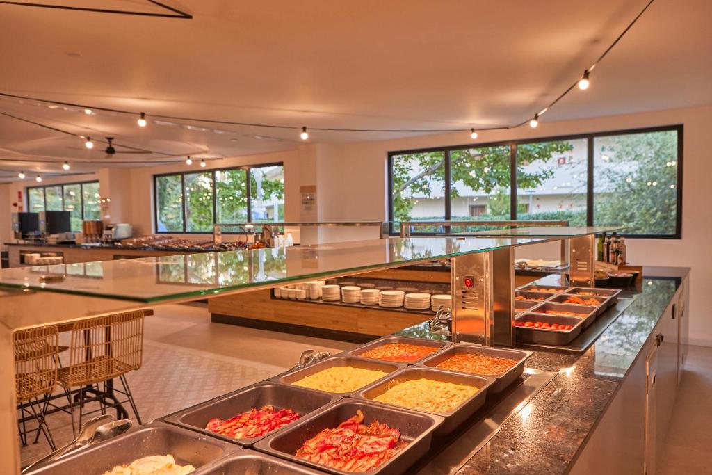Moderns ēdamzāles interjers ar bufetes stilu, kurā redzami dažādi ēdieni un plaši logi, kas sniedz dabu. Iekārtots ar elegantiem krēsliem un glītu dizainu.