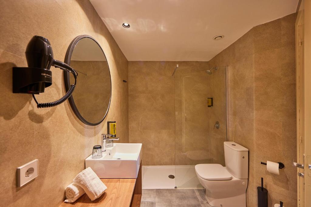Mūsdienīgs vannas istabas interjers ar dušu, izlietni un tualeti, papildināts ar matu žāvētāju un elegantu spoguli. Siltas krāsas un minimālistisks dizains rada patīkamu atmosfēru.
