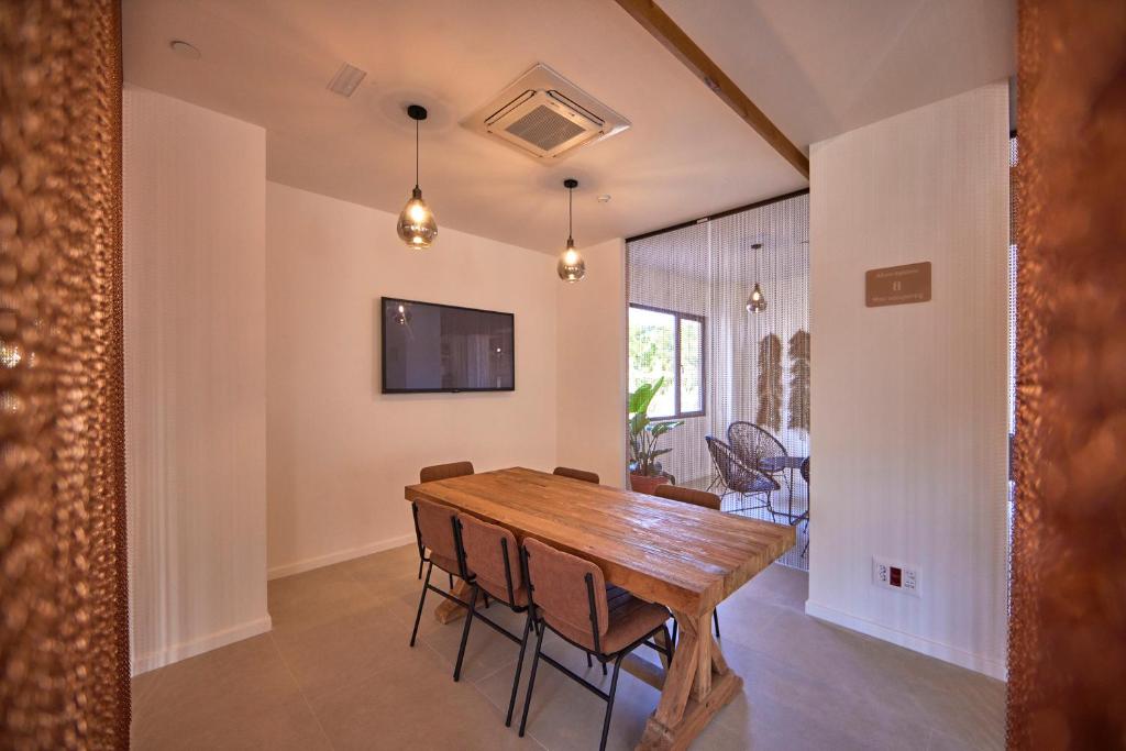 Mūsdienīga ēdamzāle ar koka galdu un metalizētām lampām, kurā ir televizors pie sienas un augu rotājumi. Telpa ir gaiša un gaumīga, radot patīkamu atmosfēru.