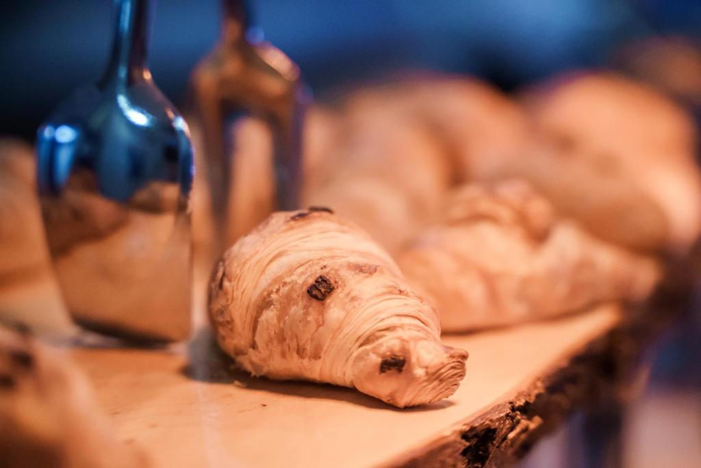 Svaigi cepti kruasāni uz koka plaukta, ar spīdīgu metāla rīku blakus.