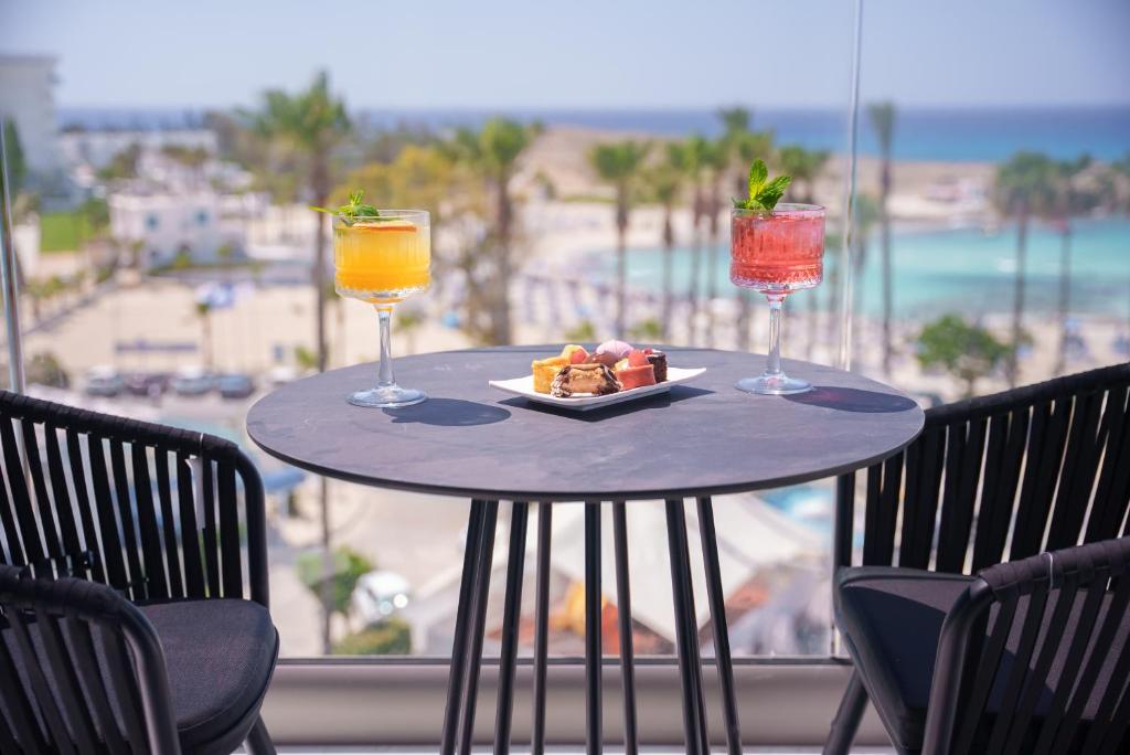 Bāra galds ar krāsainiem kokteiļiem un desertu, baudot skatu uz pludmali un palmām. Ideāla viesnīcas terase relaksācijai.