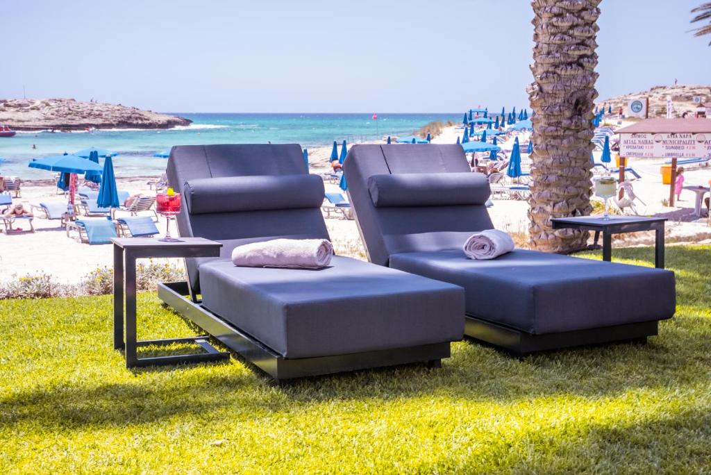 Divas modernas saulessargāšanas gultas ar spilveniem un viesmīlīgu galdiņu, blakus pludmalei ar zilu jūru un sauļošanās krēsliem. Ideāla vieta atpūtai un relaksācijai pludmalē.