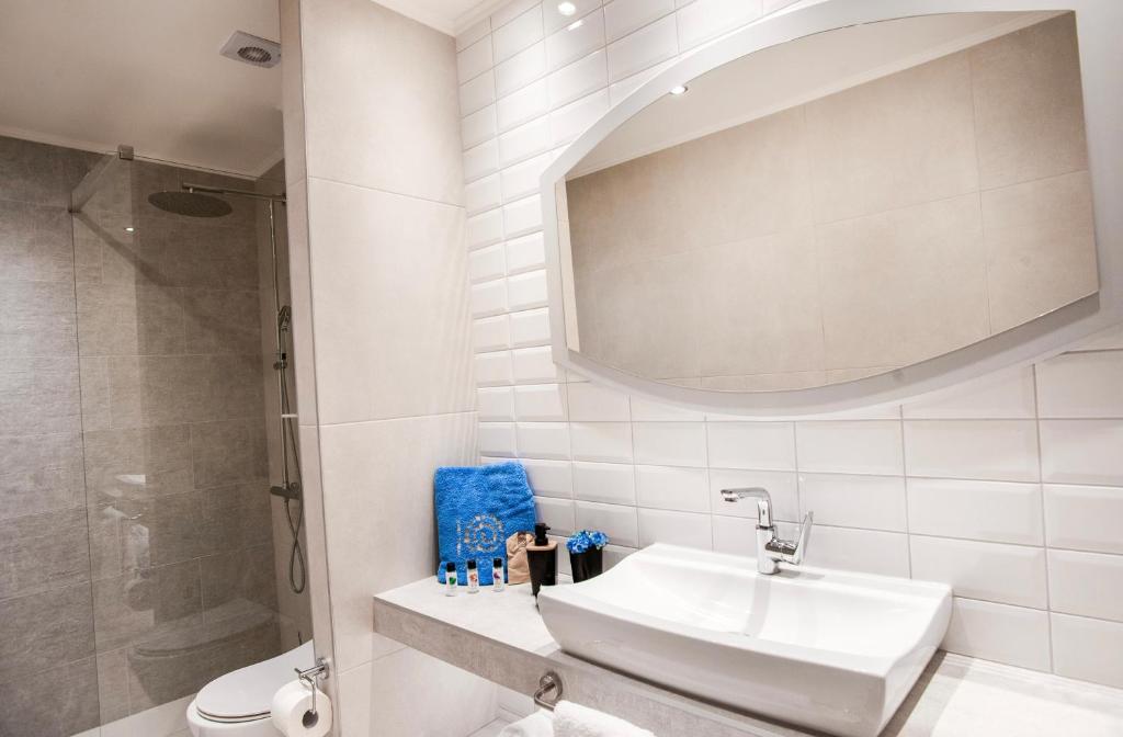 Mūsdienīgs vannas istabas interjers ar stikla dušu, pelēkām flīzēm un elegantu izlietni, kas papildināta ar zilu dvieli un kosmētikas produktiem.