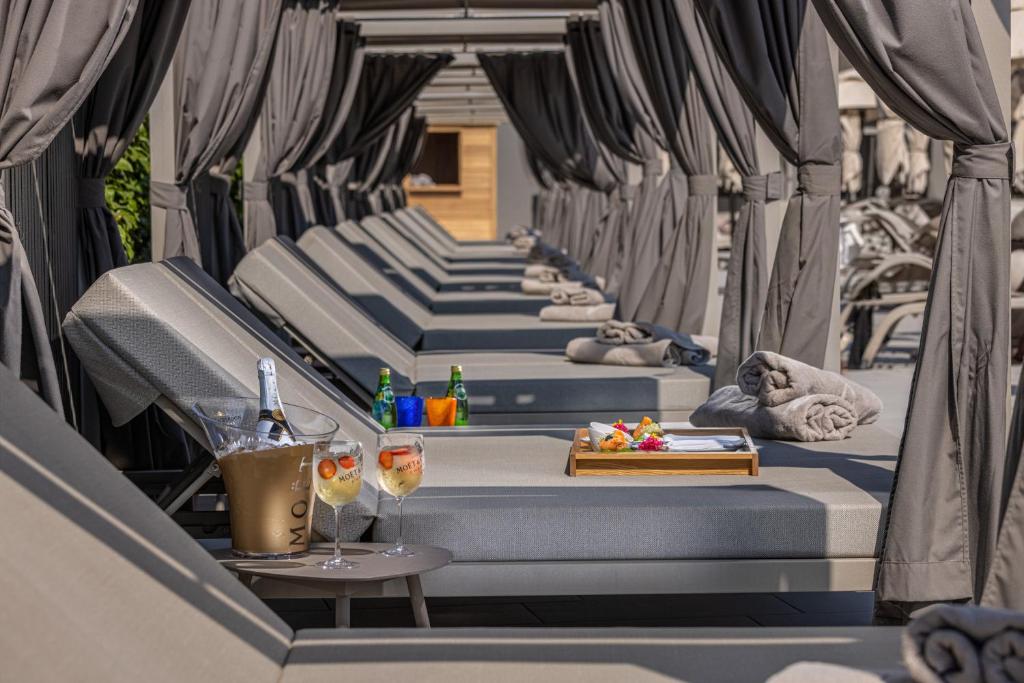 Mūsdienīgs atpūtas zona ar sauļošanās krēsliem, kas pasargāti ar pelēkām aizkulītēm, un galdiņš ar šampanieti un augļu dzērieniem, radot relaksējošu atmosfēru.