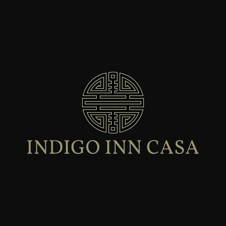 Mūsdienīgs logo ar stilizētu simbolu un nosaukumu "Indigo Inn Casa". Logo ir veidots tumšā fonā ar zeltītiem elementiem, kas piešķir elegantu un moderno izskatu.