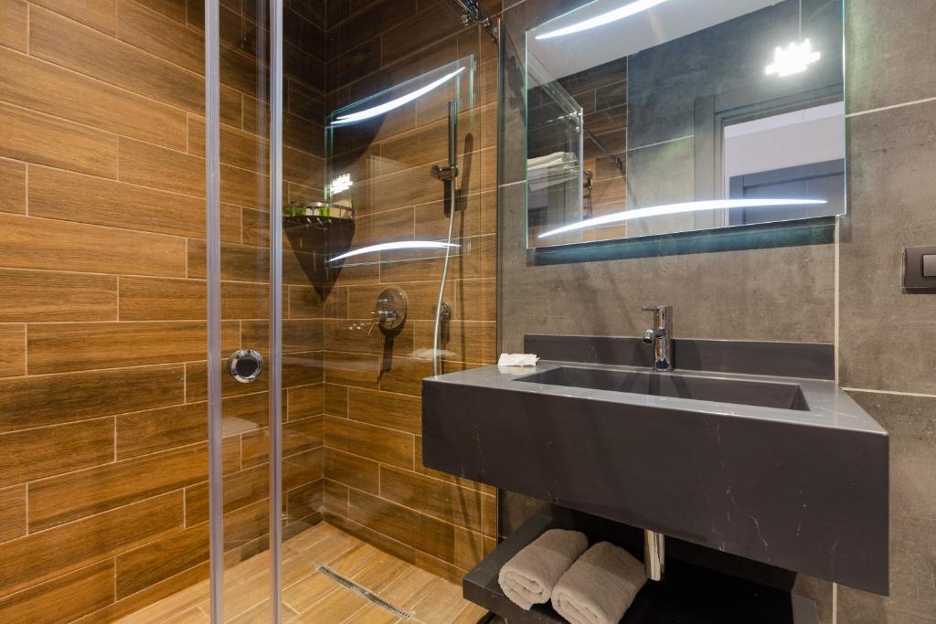 Mūsdienīgs vannas istabas dizains ar stikla dušu un melnu izlietni, kas papildināta ar koka un akmens apdari. Gaismas elementi piešķir telpai siltumu un komfortu.