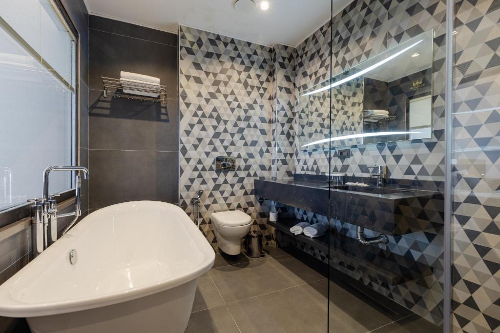 Mūsdienīga vannasistaba ar ģeometriskām flīzēm, brīvi stāvošu vannu un stikla dušas kabīni. Elegants melns izlietne un spogulis ar apgaismojumu piešķir telpai stilīgu izskatu.