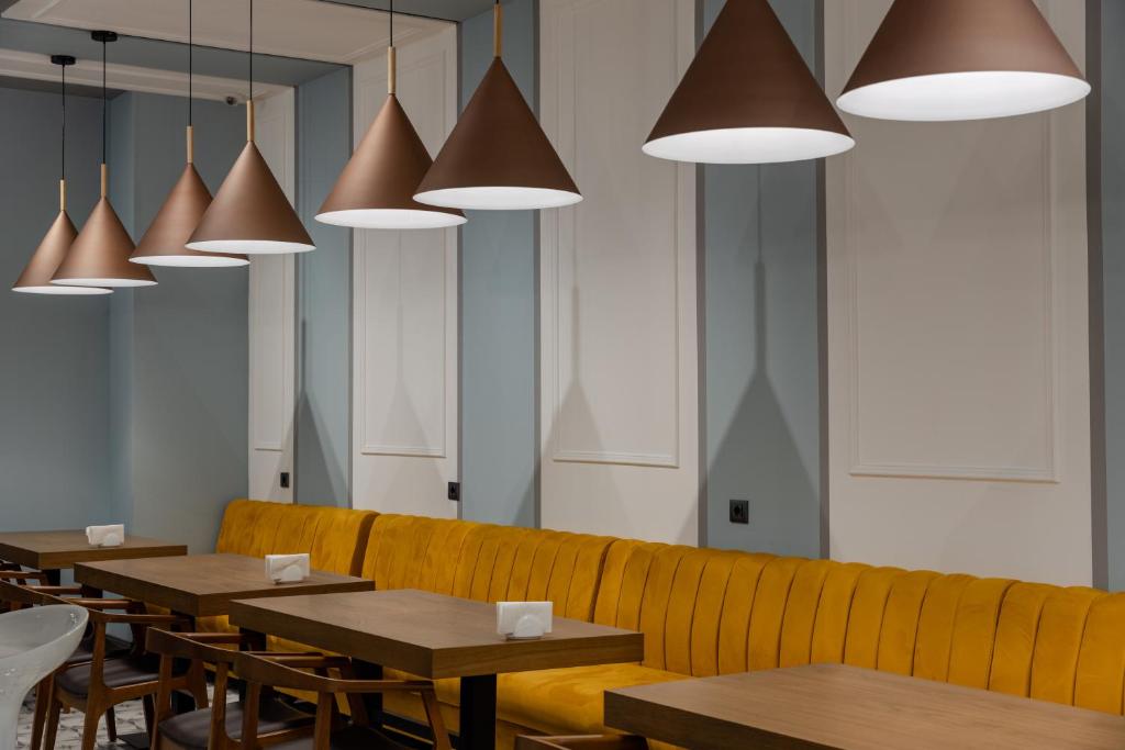 Moderns kafejnīcas interjers ar dzeltenu dīvānu, koka galdiem un stilīgām konusveida lampām. Gaismas radītais siltais tonis piešķir viesmīlīgu atmosfēru.
