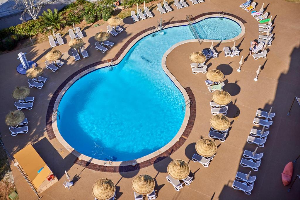 Peldbaseins ar saulessargiem un atpūtas krēsliem, kas izvietoti ap tā malu, veido relaksējošu atpūtas vidi. Skats no augšas atspoguļo peldēšanas zonu un apkārtējo teritoriju.