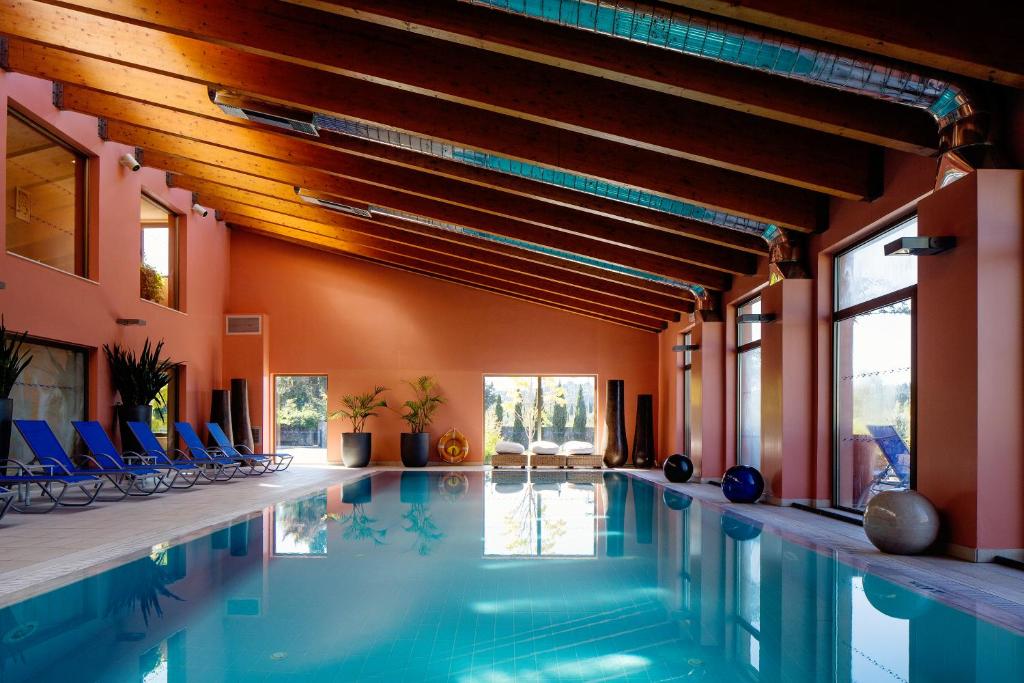 Iekštelpu peldbaseins ar mūsdienīgu interjeru, koka siju griestiem un zilu sauļošanās krēslu rindām. Telpā ir daudz dabiskās gaismas un augi, radot relaksējošu atmosfēru.