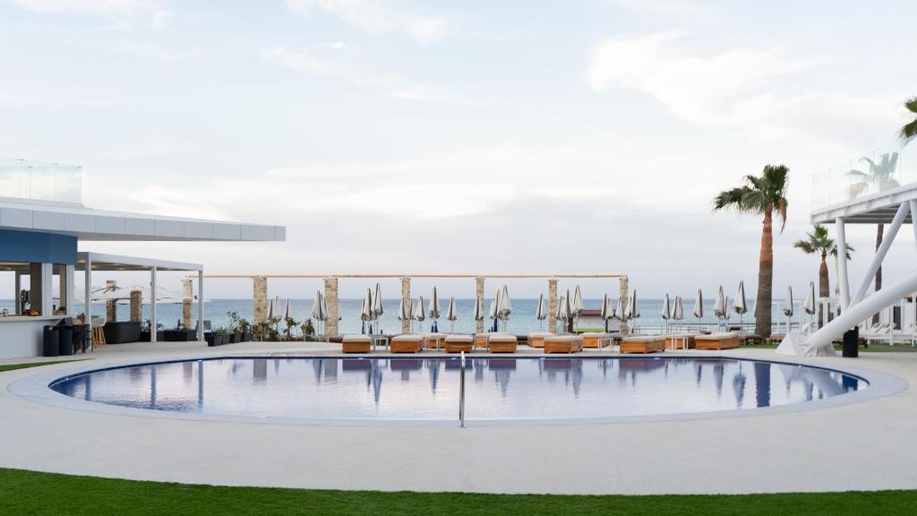 Luksusa viesnīcas baseins ar skatu uz jūru un saulessargiem. Mūsdienīga arhitektūra un zaļā zāle papildina relaksējošu atmosfēru.