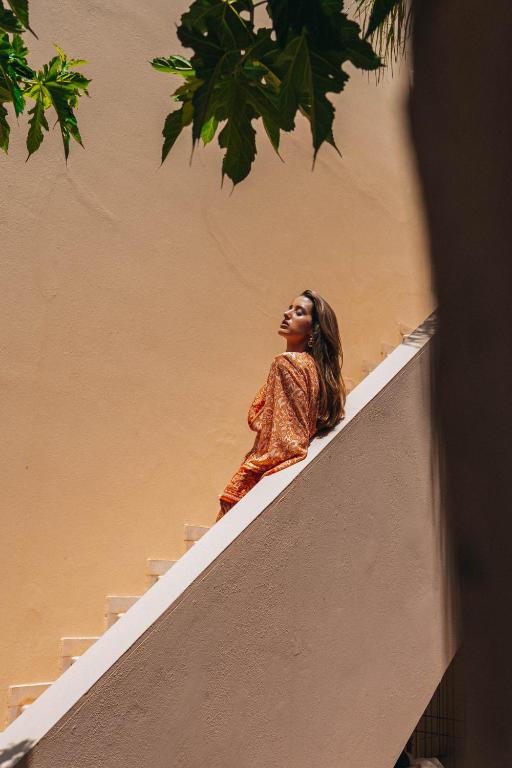 Sieviete soļo pa kāpnēm ar oranžu apģērbu, izceļoties uz dzeltena fona. Dabas elementi, piemēram, zaļas lapas, piešķir attēlam dzīvīgumu.