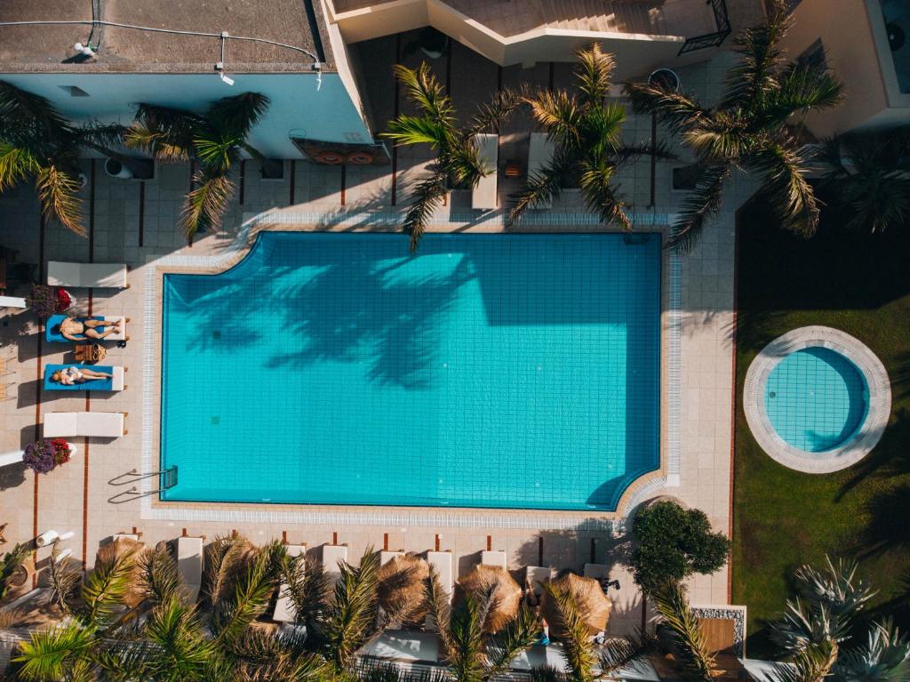 Baseins ar skaidru ūdeni un saulessargiem, ko ieskauj palmas. Redzama arī burbuļvanna un atpūtas zonas ar sauļošanās krēsliem.