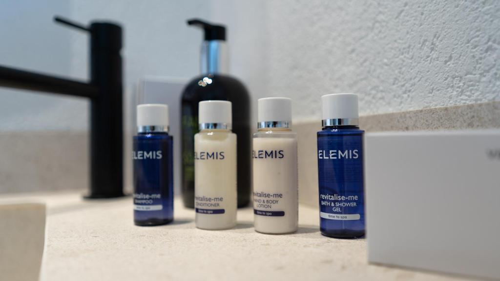 Kosmētikas līdzekļu komplekts no ELEMIS, ieskaitot šampūnu, kondicionieri, ķermeņa losjonu un vannas želeju, novietots uz vannas istabas galda.