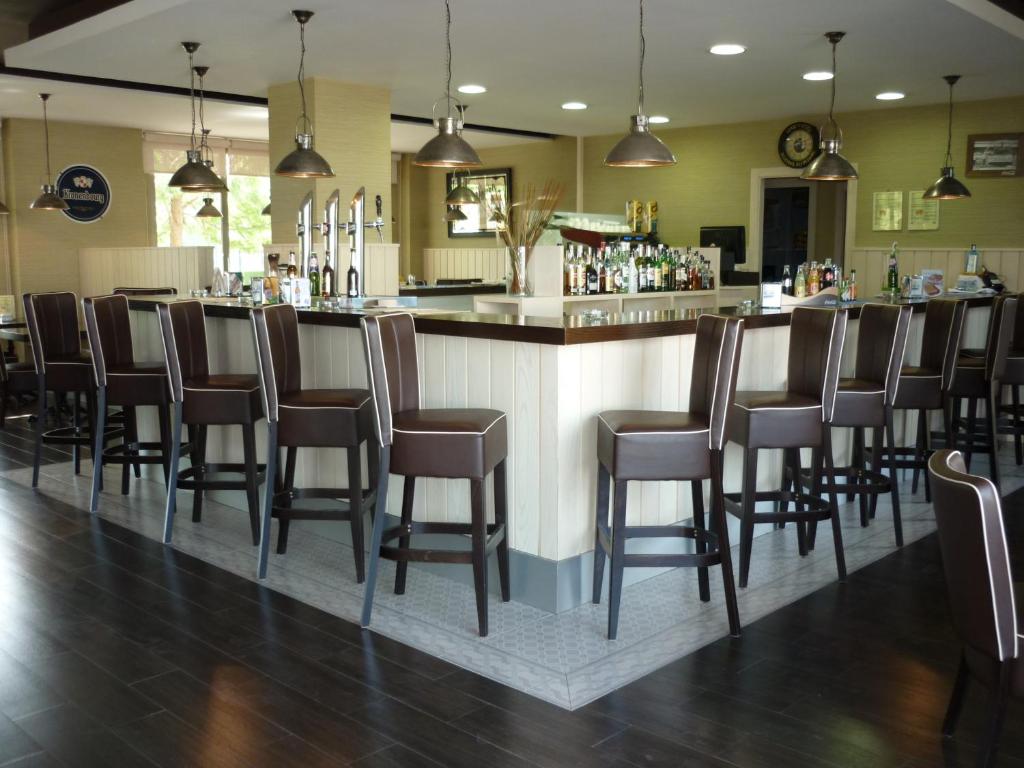 Mūsdienīgs bārs ar elegantiem koka krēsliem un glītu interjeru, kurā ir redzams plašs dzērienu klāsts. Apgaismojums rada patīkamu atmosfēru.