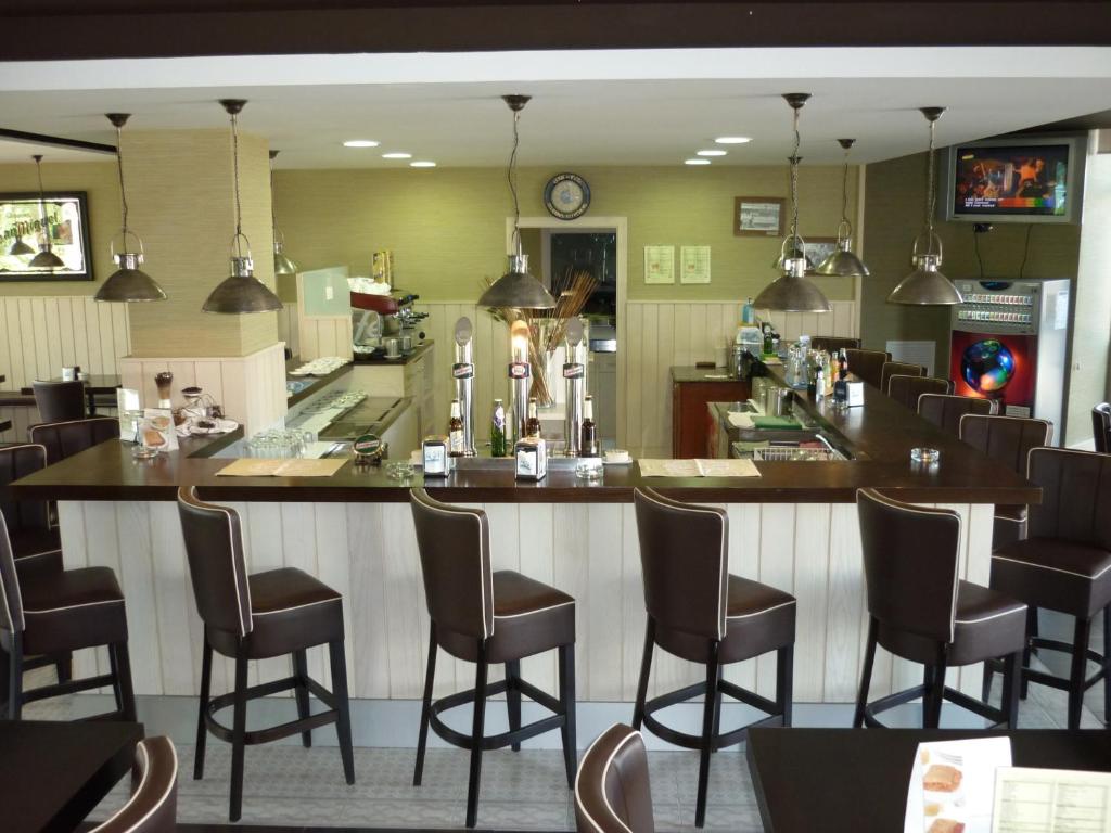 Moderns bārs ar elegantiem krēsliem un labi aprīkotu bāra letni, kurā redzami dažādi dzērienu izstrādājumi. Gaismas un interjers rada patīkamu atmosfēru.