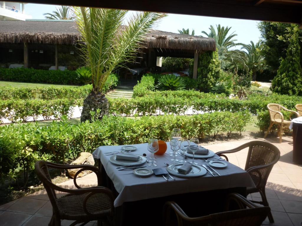 Elegantā restorāna terase ar galdu un skatu uz zaļo dārzu. Uz galda ir saklāti galda piederumi un glāzes, radot relaksējošu atmosfēru.