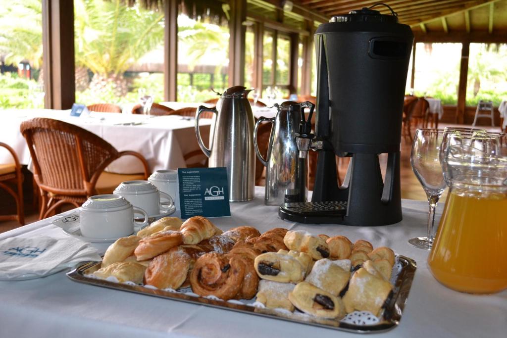 Broka veids ar kafiju un dažādiem konditorejas izstrādājumiem, piemēram, cepumiem un pīrādziņiem, uz galda restorānā ar zaļojošiem skatiem pa logu.