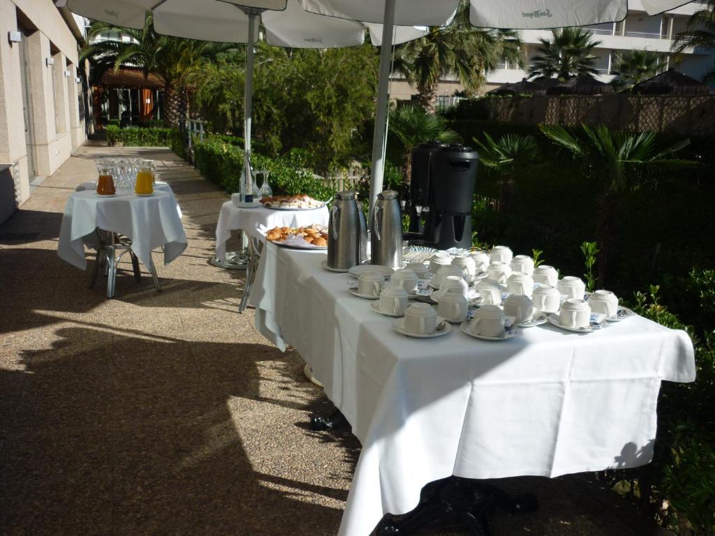 Brokastu galds ārpus telpām ar kafiju, tēju un uzkodu izvēli, apzaļumots apkārtējais ainava.