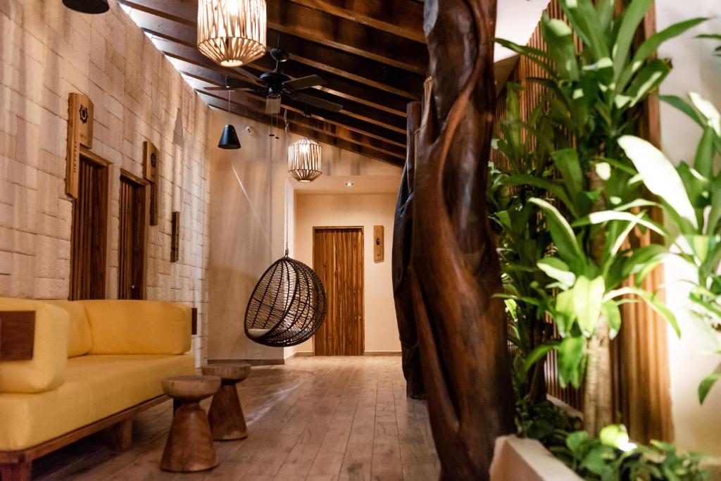 Mūsdienīgs interjers ar dzeltenu dīvānu, vītnes gaismas, atpūtas krēslu un zaļām augu kompozīcijām, radot mierīgu atmosfēru.