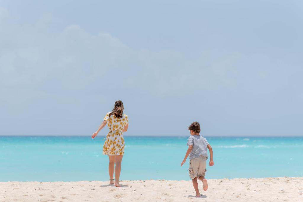 Bērns skrien pa pludmali, kamēr sieviete ar ziedu rakstu kleitu stāv un skatās uz jūru. Aizraujošs vasaras mirklis pie ūdens.